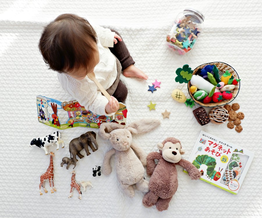 Kind sitzt auf einer Decke, umgeben von Spielsachen