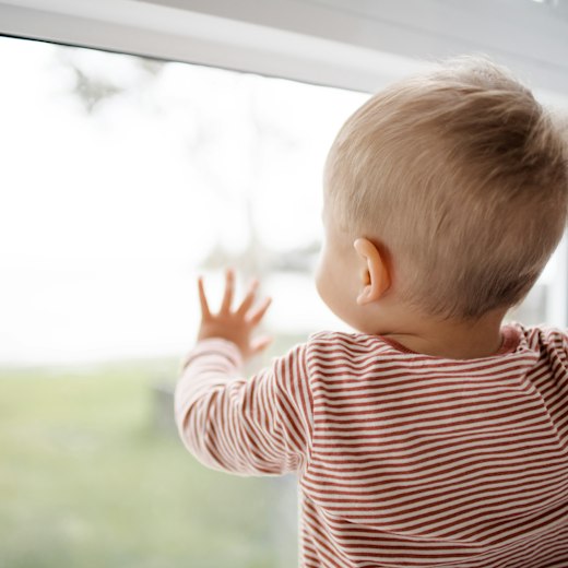 Kleinkind steht im Morgenlicht am Fenster